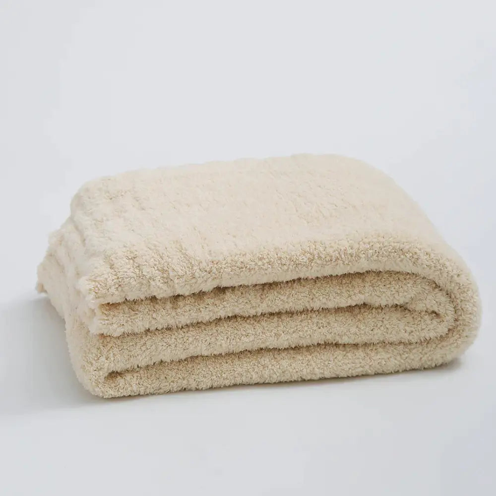 A cream knitted throw blanket made of ribbed plush microfiber neatly folded in a compact stack for bedroom use