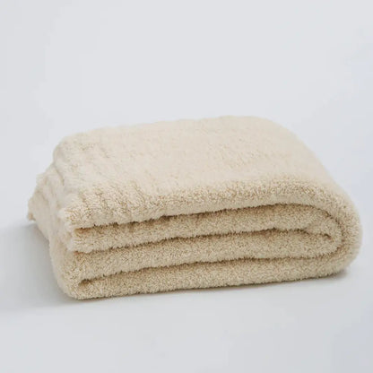 A cream knitted throw blanket made of ribbed plush microfiber neatly folded in a compact stack for bedroom use