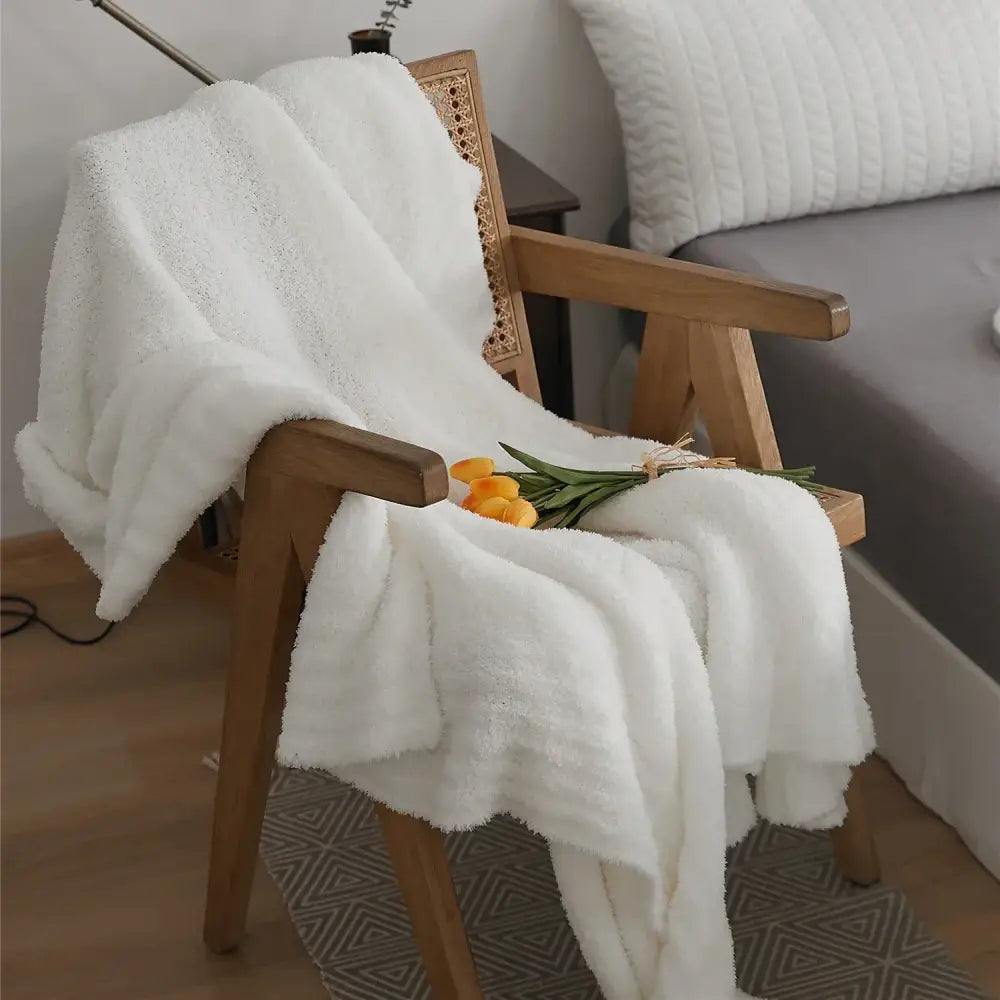 A cream knitted throw blanket in plush microfiber fleece draped over a wooden chair for bedroom use