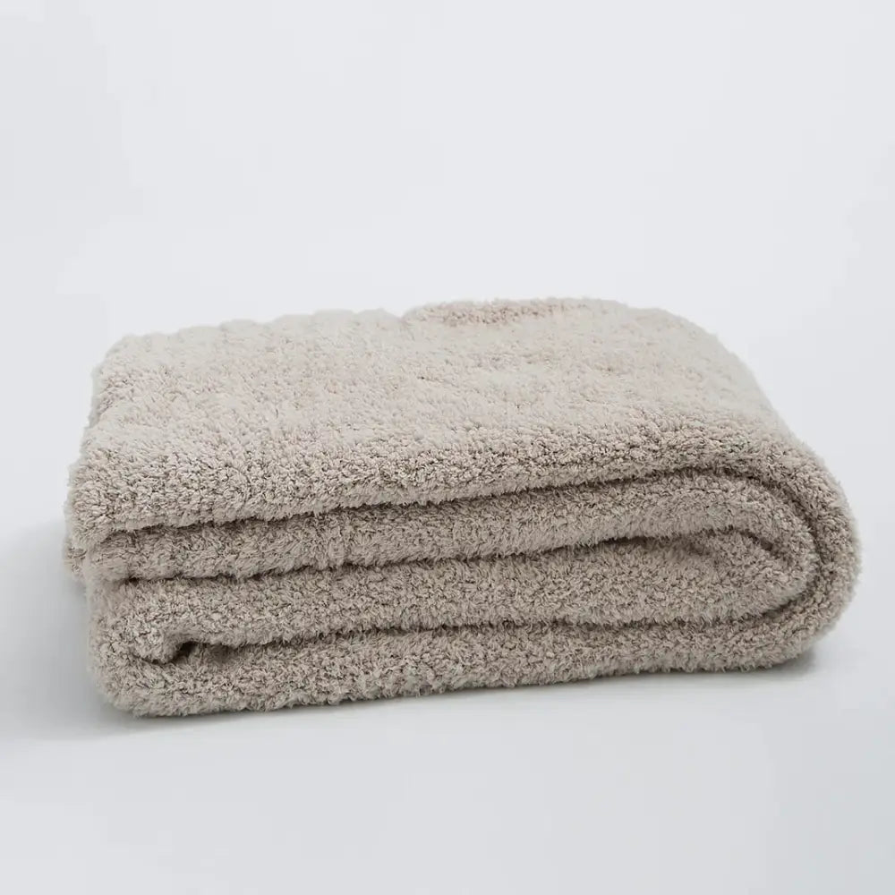 A cream knitted throw blanket with ribbed plush microfiber and a soft beige terry cloth bath towel surface