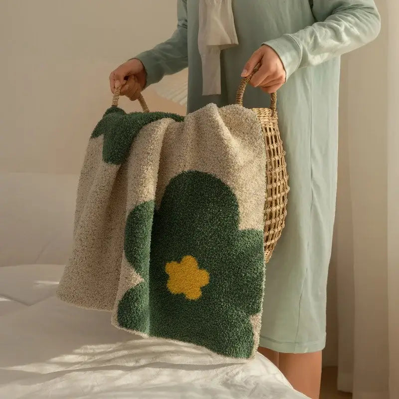 A plush cream korean kawaii flower blanket with beige green tones and yellow flower design held by woven handles