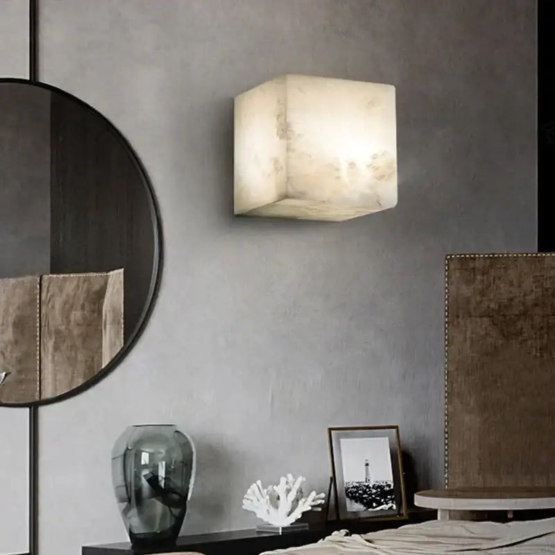 A cream onyx cube marble wall lamp with natural veining softly glowing as a decorbites cube marble sconce