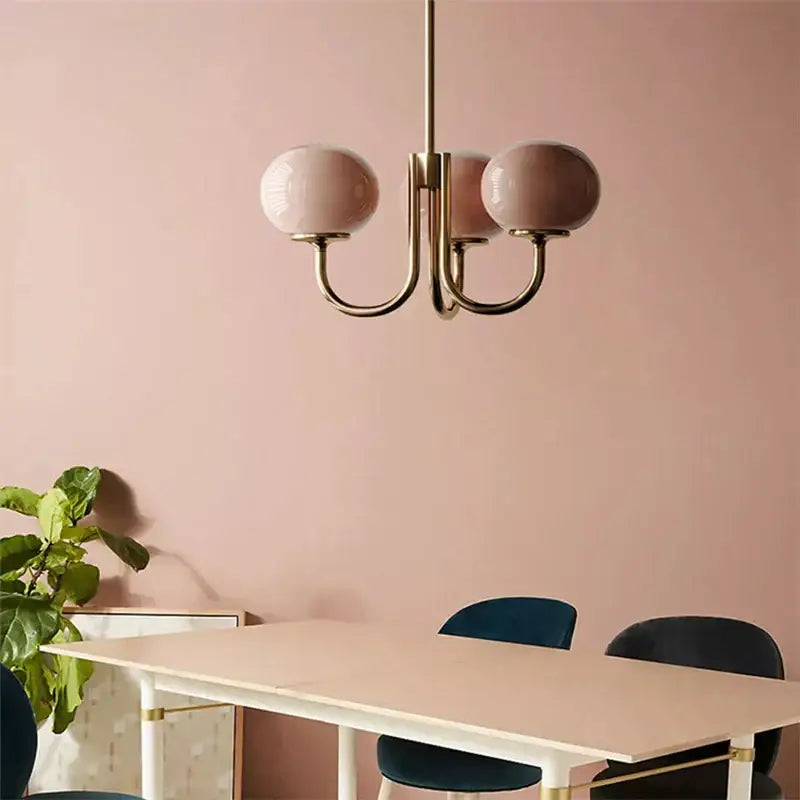 A modern cream pink bedroom pendant light with three blush pink glass globes and brass finish by decorbites