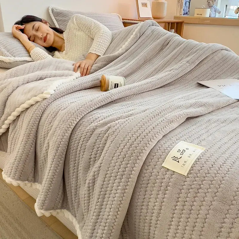 A cozy light gray double sided jacquard milk velvet throw blanket with ribbed pattern and soft white fringe edges
