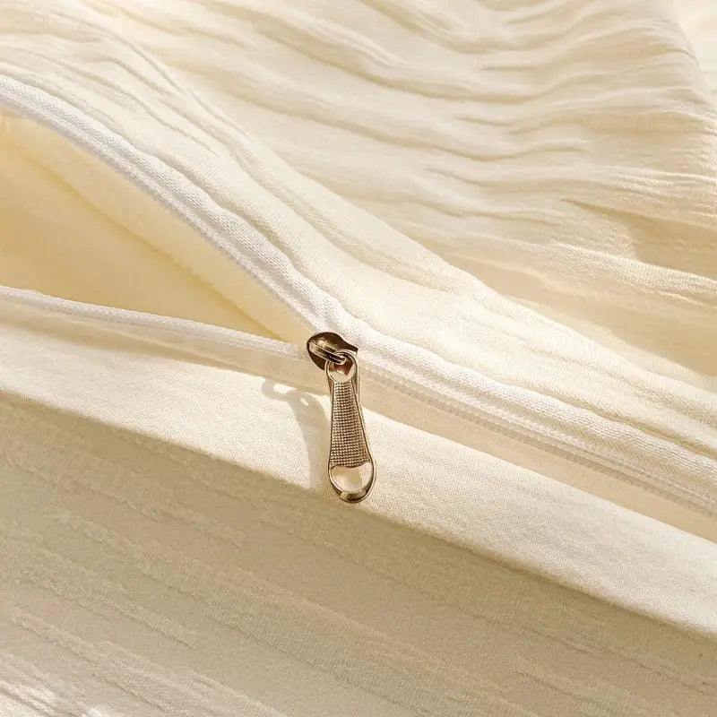 A gold-toned textured zipper pull on a cream ribbed bubble yarn fabric of a duvet cover set for bedroom bedding