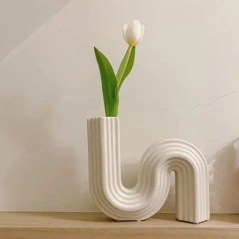 A cream ribbed geometric ceramic vase in s shape holds a single white tulip for living room decorbites geometric decor