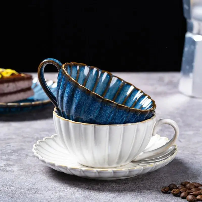 A deep blue ceramic afternoon tea cup with fluted design and gold rim in a cream scalloped ceramic afternoon saucer