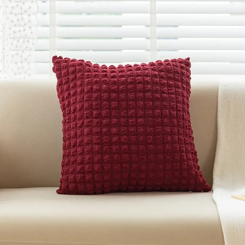 A deep red elastic puff plaid cushion cover with a textured quilted surface on a beige sofa for living room decor