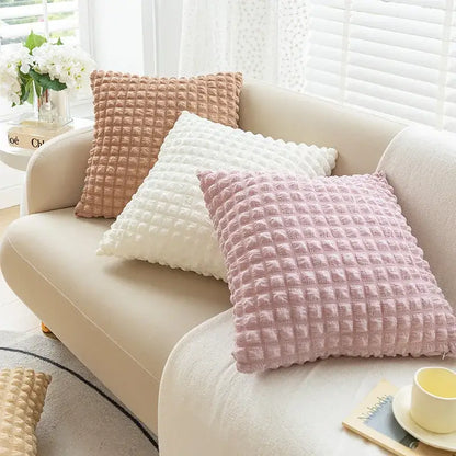 Three elastic puff plaid cushion covers in soft pink white and beige rest on a cream sofa for living room decor