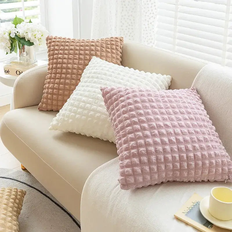 Three elastic puff plaid cushion covers in soft pink white and beige rest on a cream sofa for living room decor