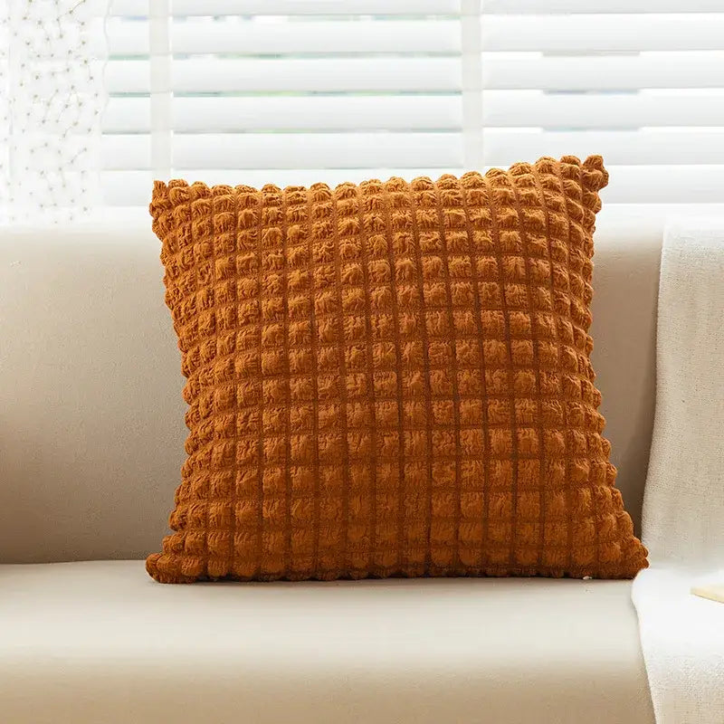 A warm orange elastic puff plaid cushion cover with raised grid texture on a light sofa for living room decor