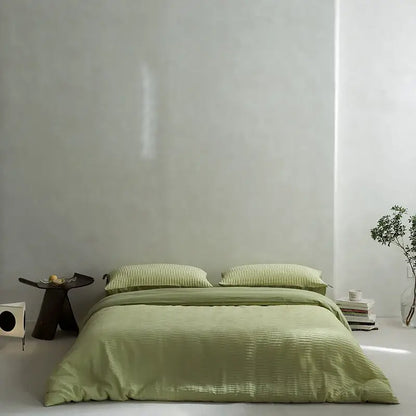 A soft sage green ribbed duvet bedding set made of cotton foam yarn with matching pillows on a minimalist bed