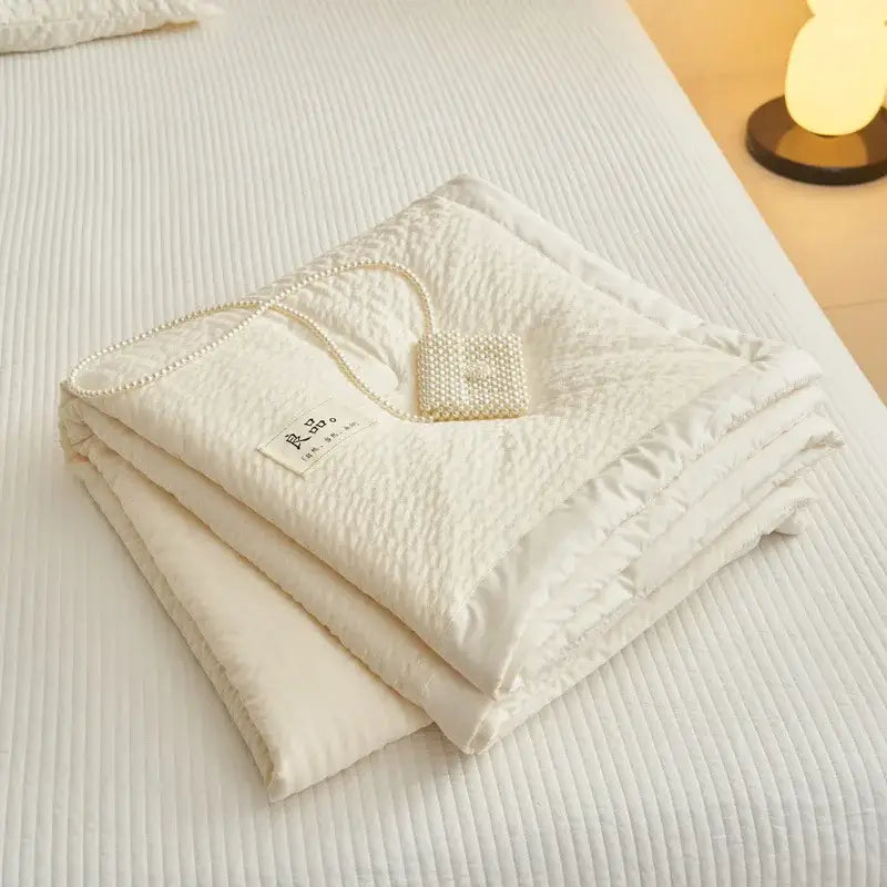 A cream textured ice cream air summer quilt with a subtle quilted surface adorned by a delicate pearl necklace