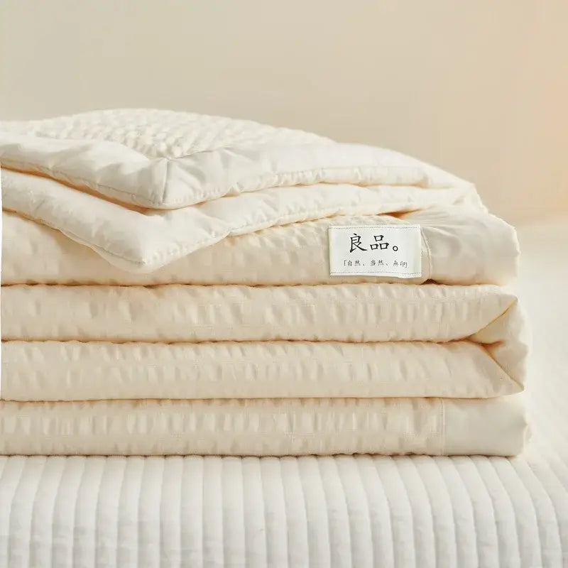 A neatly folded cream textured ice cream air bubble summer quilt with subtle pattern and chinese label by decorbites