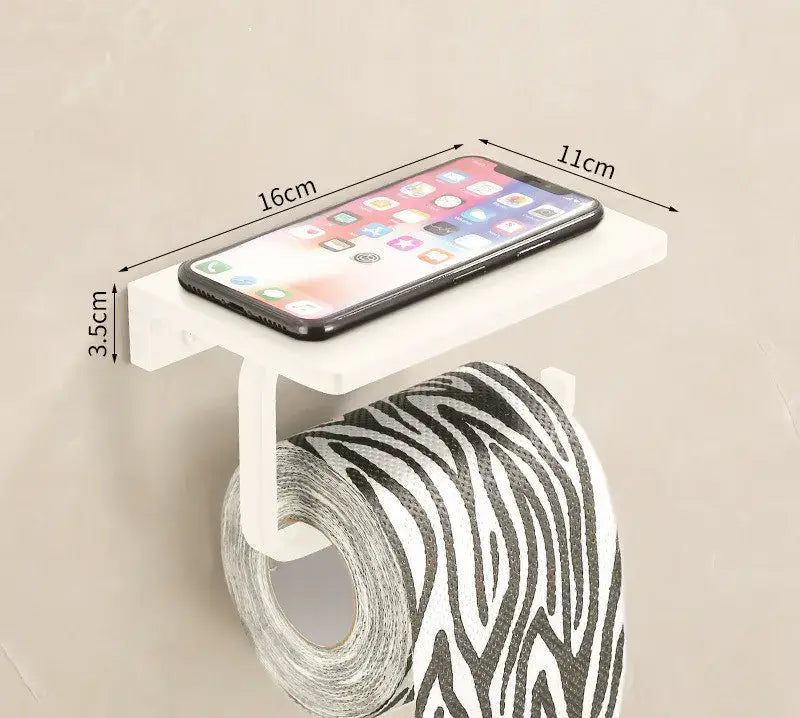 White plastic toilet paper holder with integrated phone shelf holding black smartphone in cream white bathroom set with towel rack