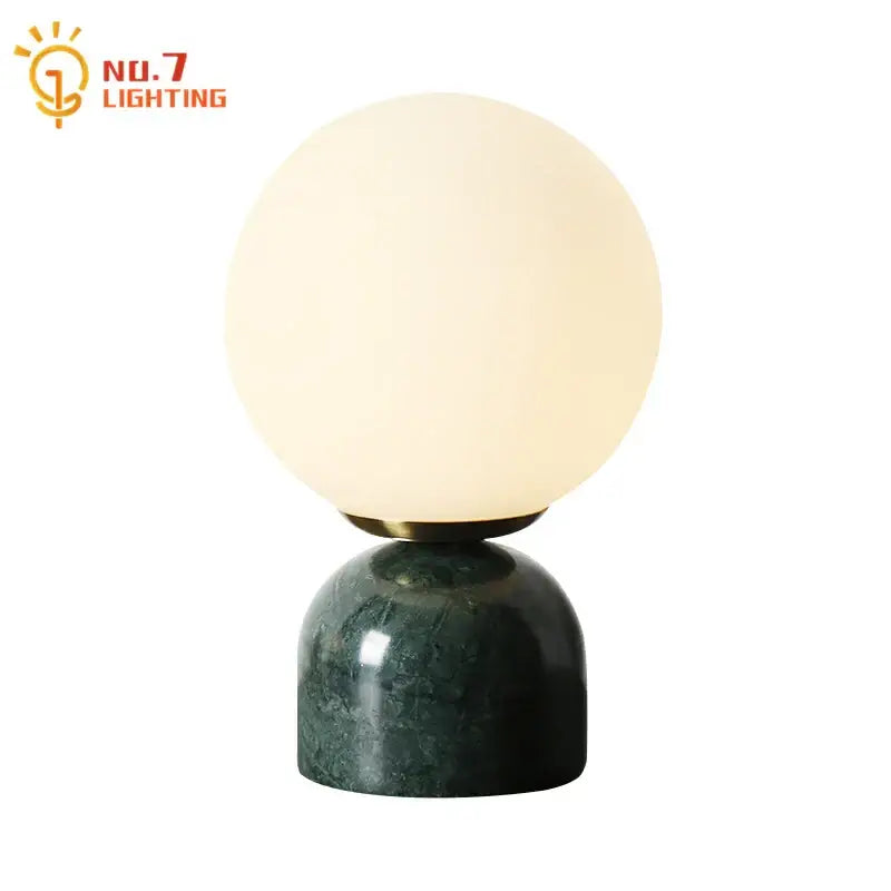 A decorbites cream wind table lamp with a spherical glass off-white globe and dark green cream wind marble base