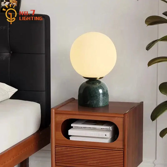 A cream wind marble table lamp with a spherical glass light and warm glow on a dark green marble base for decorbites cream wind decor