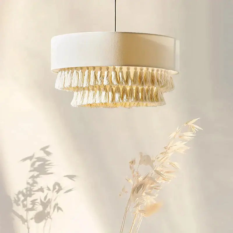 A cylindrical white fabric pendant light with layered tassels for bedroom decorbites creamy bohemian style