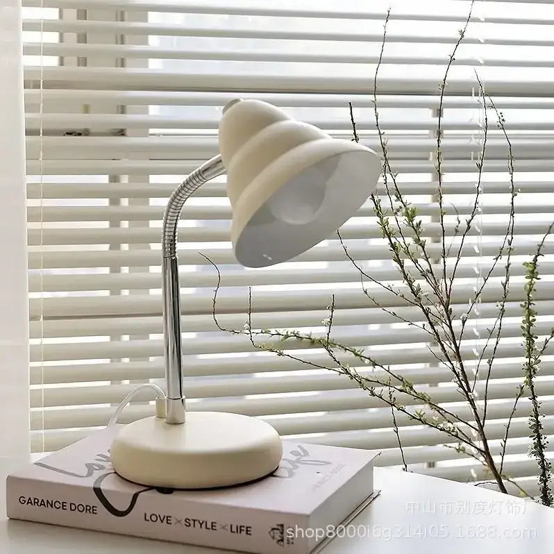 Cream-colored decorbites creamy style desk lamp with flexible chrome neck and rounded shade on a book for reading light