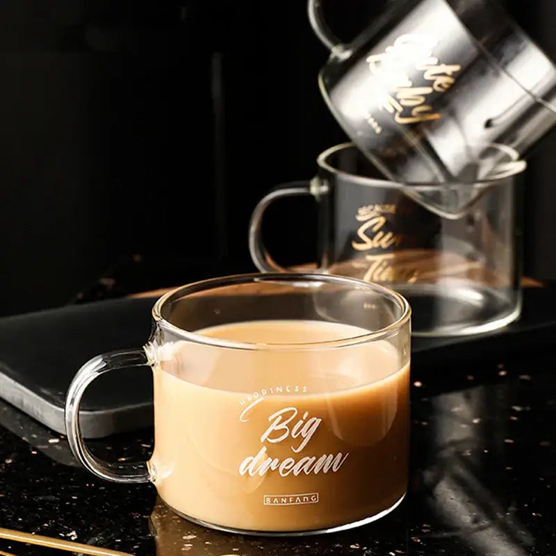Clear glass creative alphabet glass juice cup with gold big dream inscription filled with light brown beverage