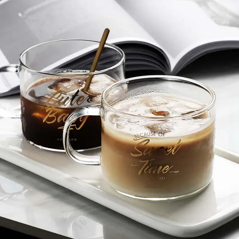 Two clear glass mugs with gold cursive lettering filled with iced coffee from decorbites creative alphabet glass series