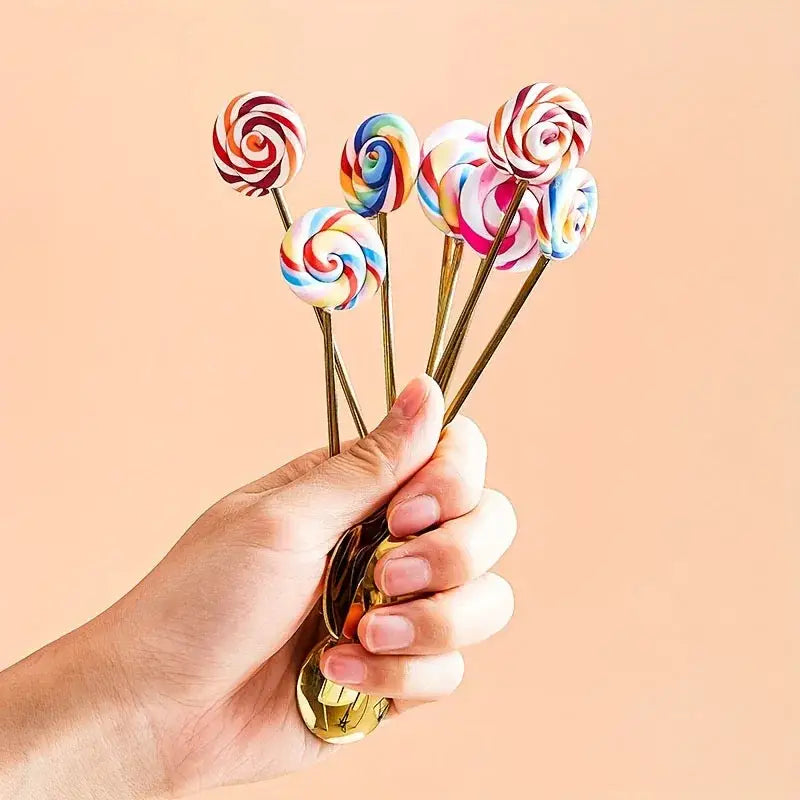 A hand holds colorful swirled lollipops with gold sticks beside a creative candy donut dessert fork and gold spoon set