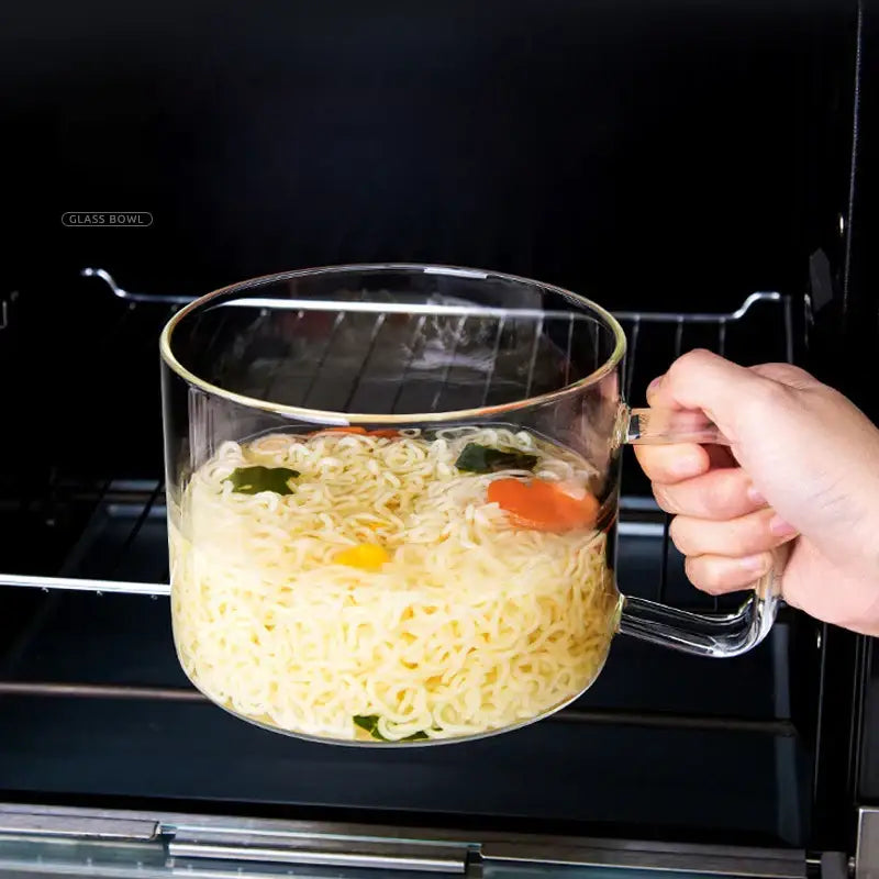 Creative clear glass salad bowl with handle containing cooked noodles and vegetables for kitchen and dining room use