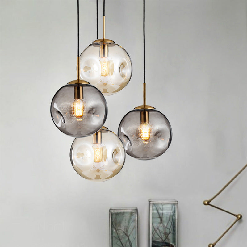 Modern glass globe pendant light with gold accents and black cords.