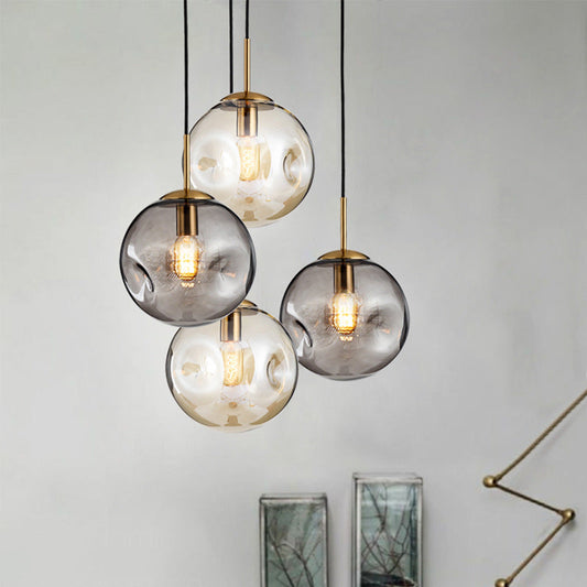 Modern glass globe pendant light with gold accents and black cords.