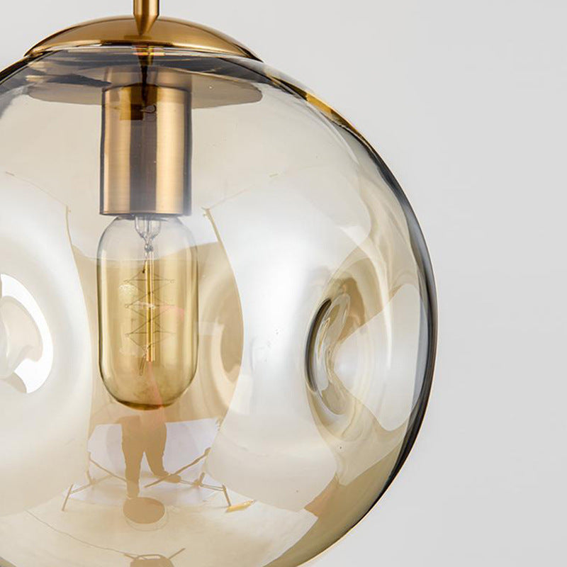 Gold globe pendant light with clear glass shade and exposed filament bulb.