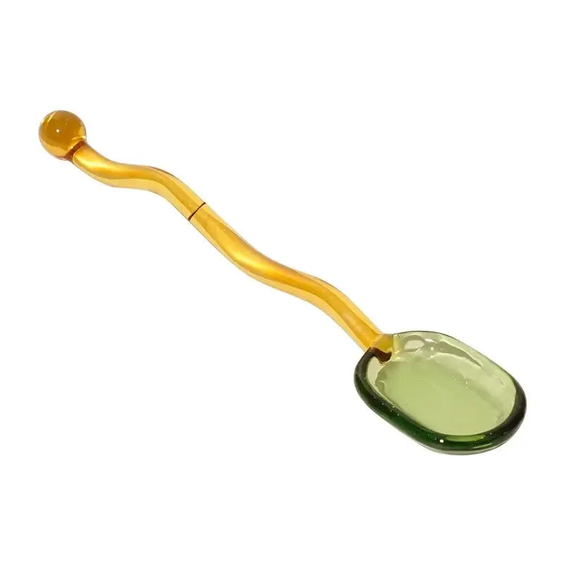 A creative glass spoon dessert with a translucent amber oval bowl and a curved green wavy handle for kitchen dining