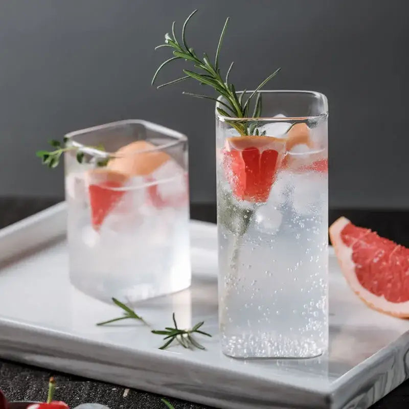 Tall clear decorbites creative square glass with gold rim filled with sparkling water garnished with grapefruit and rosemary