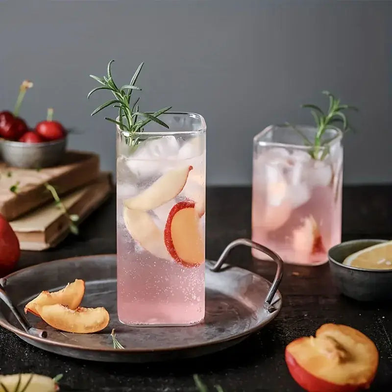 Tall clear decorbites creative square glass with gold rim filled with pink sparkling drink and fresh rosemary garnish