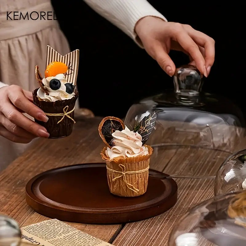 A chocolate cupcake with white frosting blueberries and a candied orange slice in a decorbites creative wooden cake storage box with glass lid