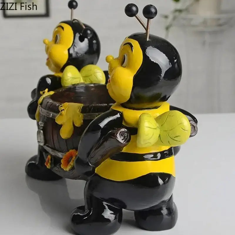 Two glossy black and yellow bee resin vases shaped as figurines holding miniature barrel planters for living room decor