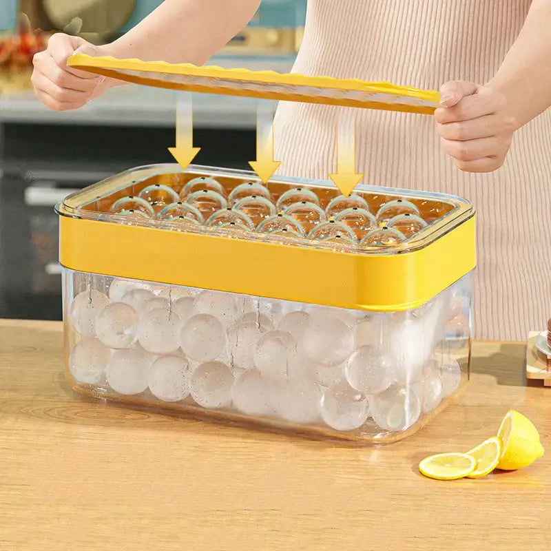 Creative yellow and clear silicone ice mould tray with lid being lifted to reveal frozen spheres inside for kitchen drink cooler