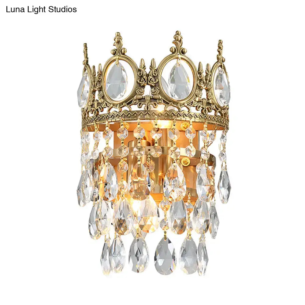 Gold-toned crown-shaped wall mounted lighting with clear crystal prisms and teardrop pendants in aged brass finish