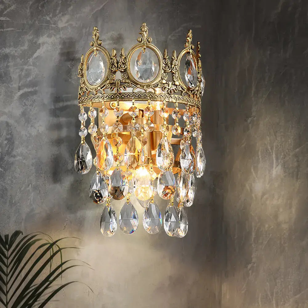 Gold-toned crown shaped wall mounted lighting with clear crystal prisms in aged brass for bedroom decor