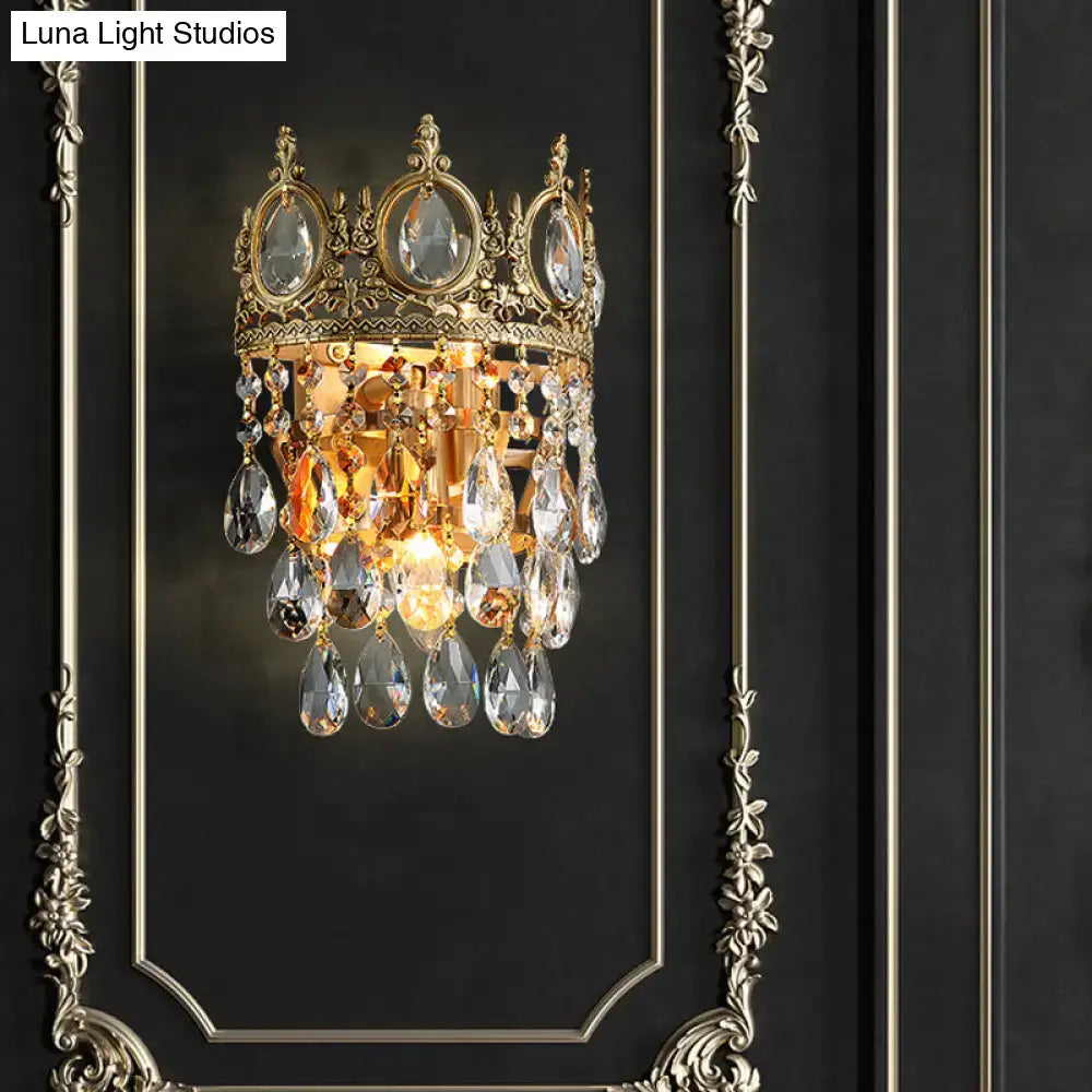Gold-toned crown-shaped round wall mounted lighting with clear crystal prisms and ornate aged brass metalwork for bedroom