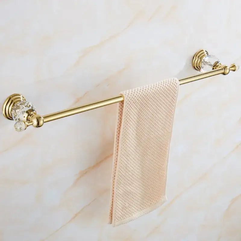 Gold-toned crystal bathroom accessories set towel rack with brass finish and crystal embellishments holding beige mesh towel