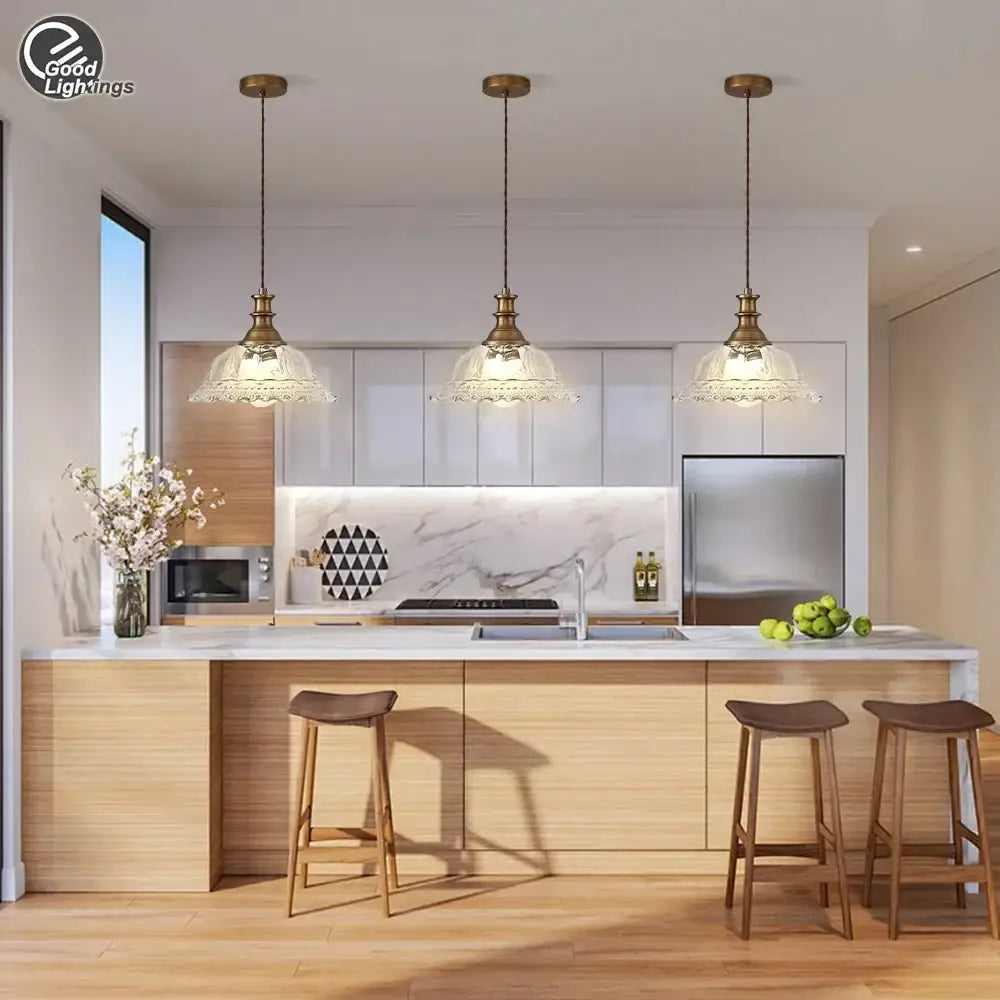 Three brass glass pendant chandelier lights with clear scalloped shades hang above a modern kitchen island