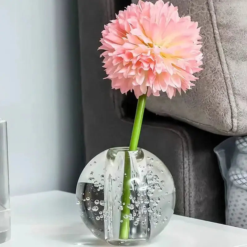 A clear textured crystal bubble ball vase with internal bubbles holding a single pink artificial flower for decorbites decor