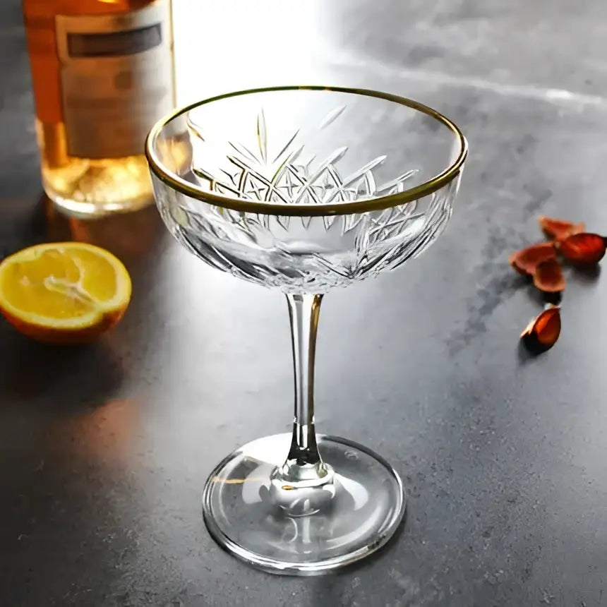 A clear crystal coupe glass with intricate cut patterns and a gold rim for decorbites gold rim coupe use