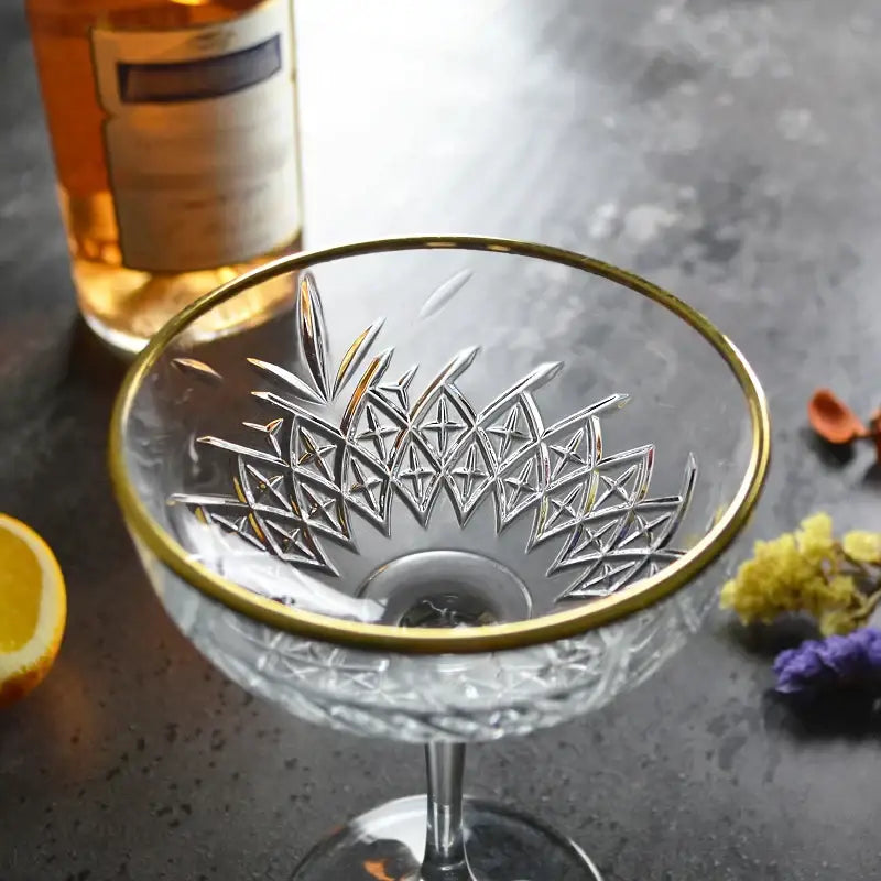 A clear crystal gold rim coupe glass with intricate geometric etching patterns for elegant cocktail use by decorbites gold rim
