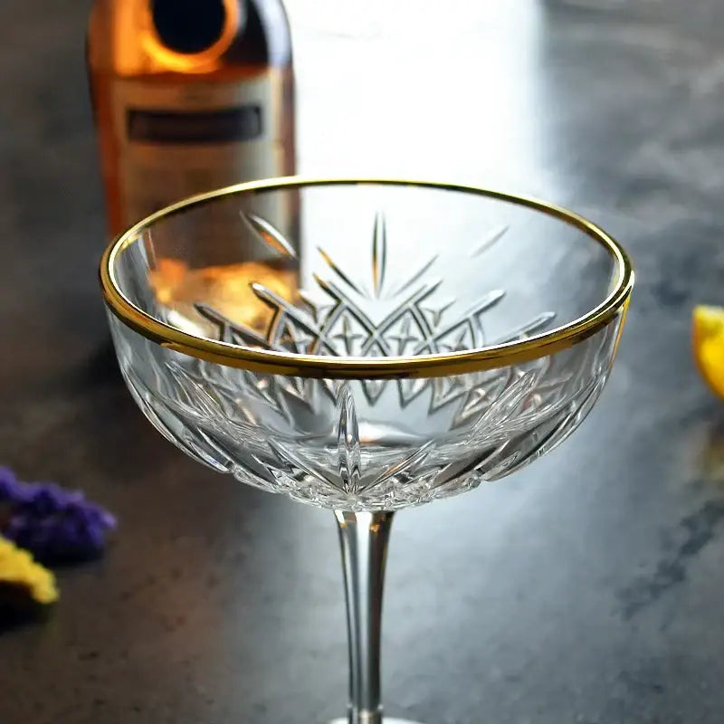 A clear crystal coupe glass with gold rim and intricate cut-glass patterns ideal for decorbites gold rim collections