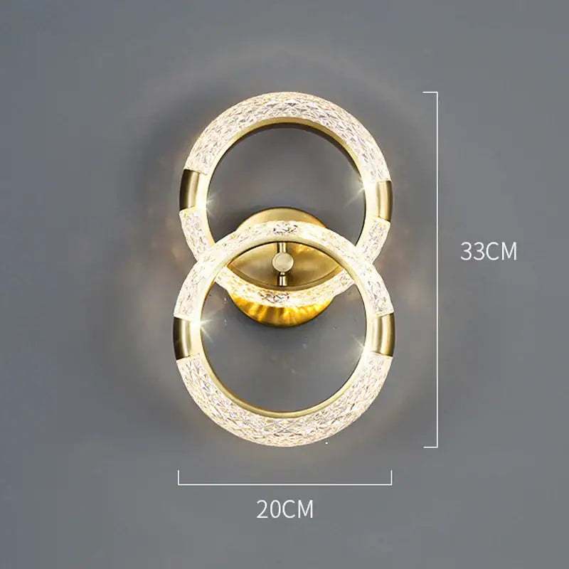 Gold-toned decorbites crystal nordic wall sconce with two interlocking rings and sparkling crystal accents for bedroom light