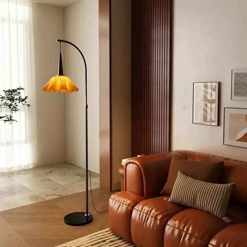 A sleek black floor lamp with a curved neck and amber petal shade beside a living room floor shelf