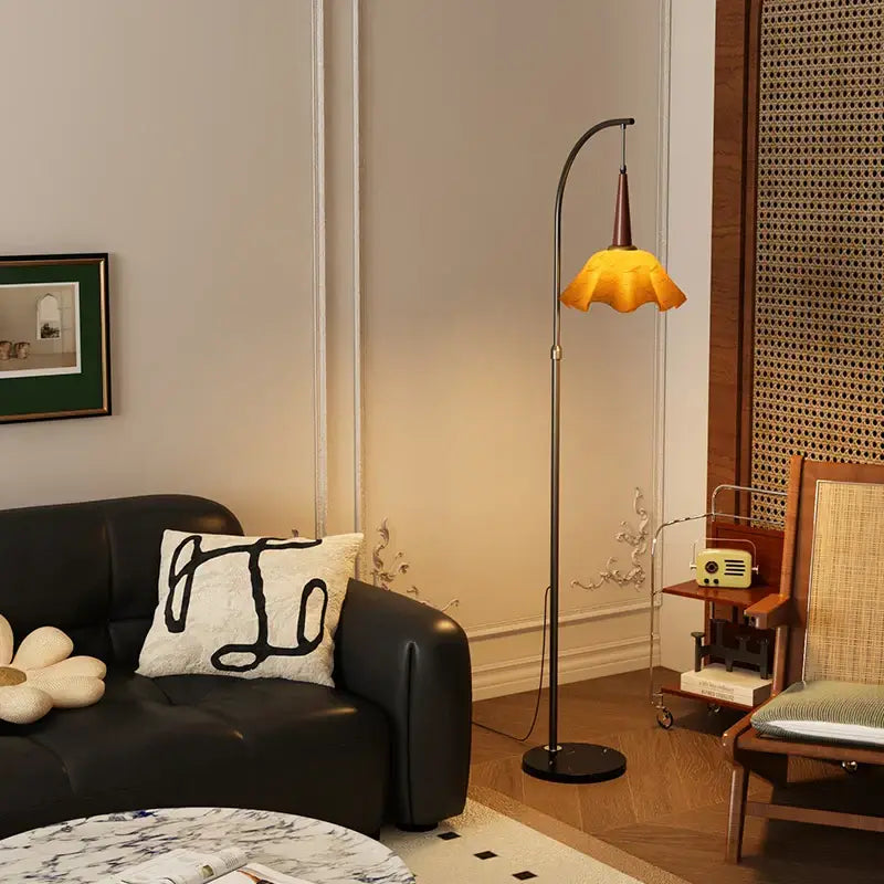 Vintage-style floor lamp with curved black metal stand and amber petal shade next to living room floor shelf