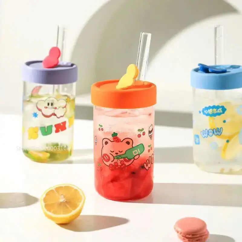 A vibrant red glass cup with a decorbites cartoon bear design, orange lid, and clear straw with yellow heart charm