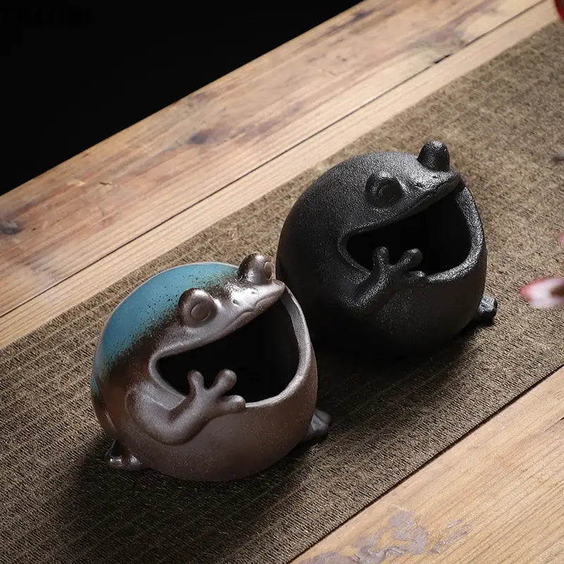 Two ceramic ashtrays featuring cute big belly frog designs in blue brown glaze and matte black for living room decor